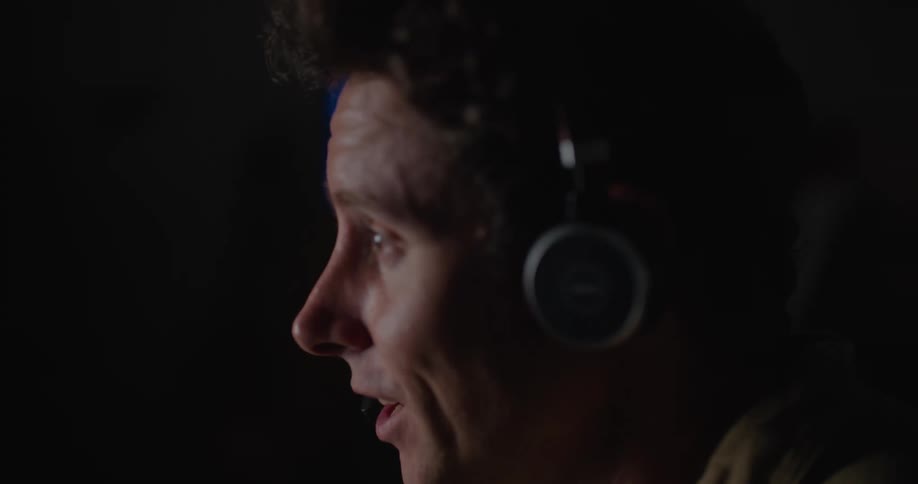 A man talks into a headset while sitting in a dark room