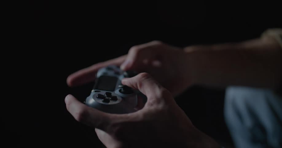 Man sits in dark room talking via headset as he manipulates a game controller