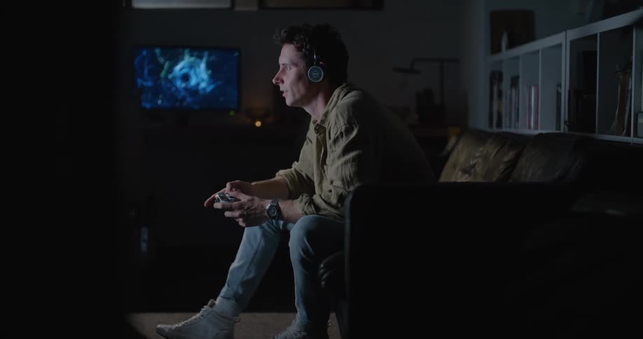 Man wearing a headset sitting at the couch and playing video game