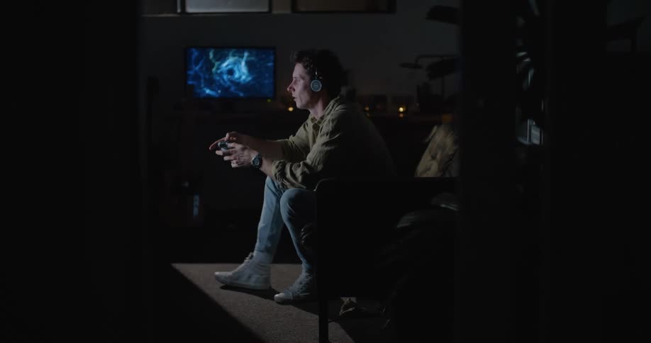 An adult male sits on his couch and seems frustrated while playing a video game