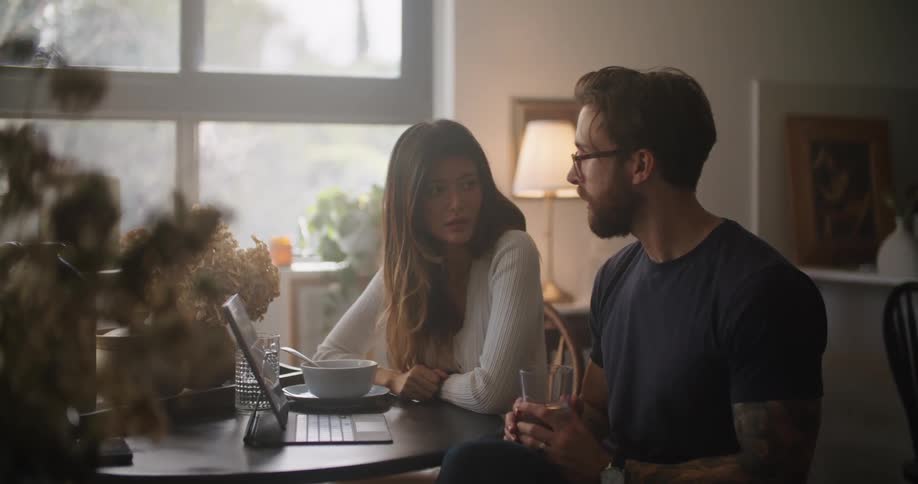 Man and woman sitting at the table talking about something showing on the laptop screen