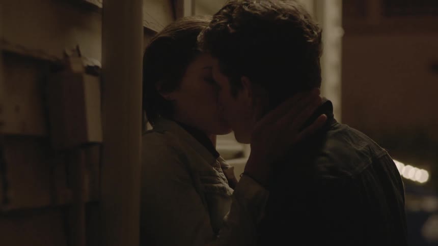 A man and woman kiss by the side of a home