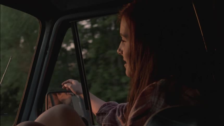 A woman is smiling as she rides in a car and waves her arm out the window