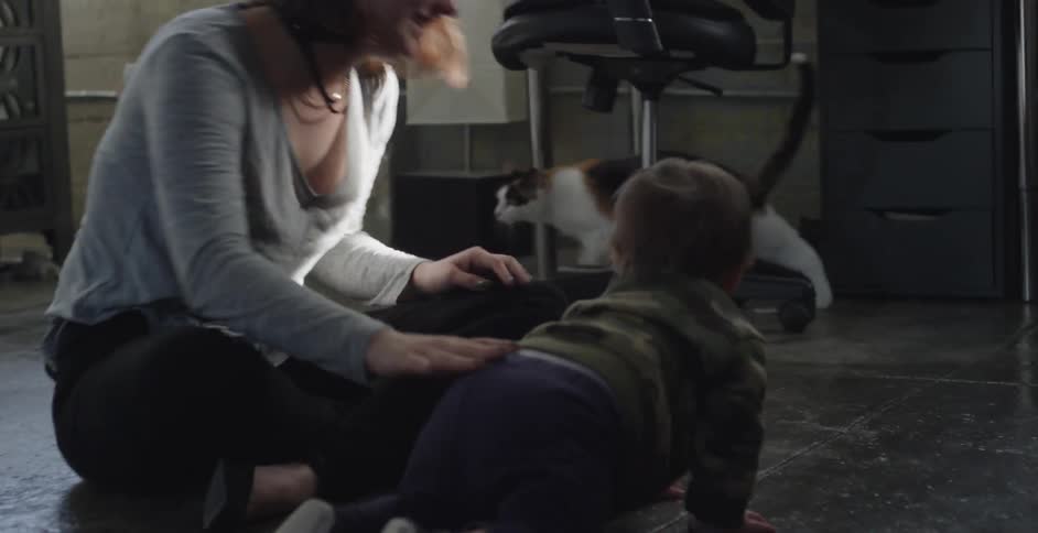 Woman sitting down and picking up her infant as its crawling towards a cat