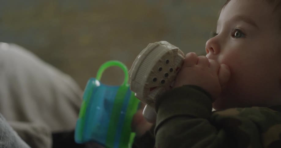 A baby puts a toy in his mouth while holding another above his shoulder