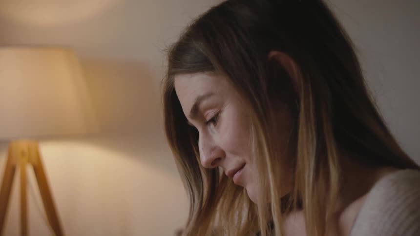 Pregnant woman with brown wavy hair sits on bed and looks at photograph in bedroom