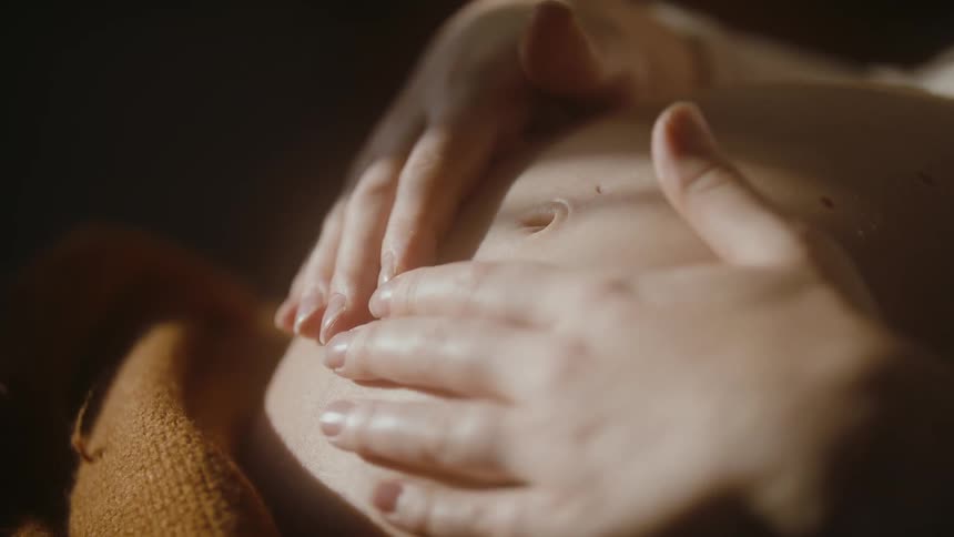 A woman massages her pregnant belly with both hands