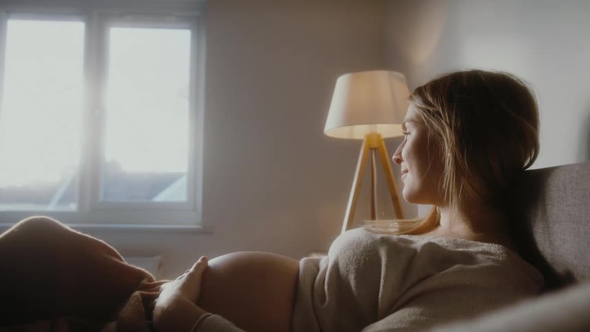 A pregnant woman lays in bed rubbing her belly