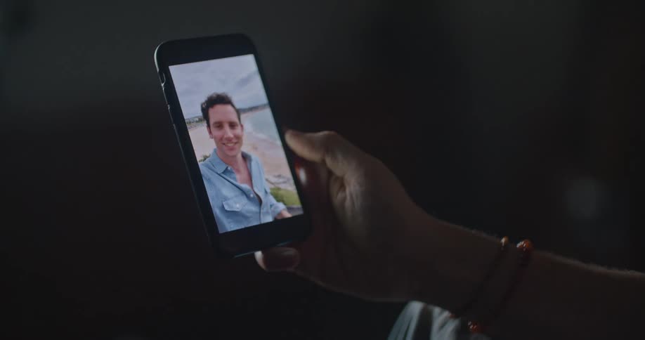 Man with wristband holds smartphone making video call with man on the beach