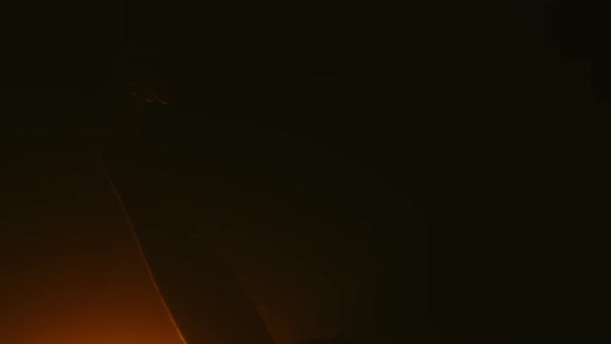 Woman sitting in dark room dimly lit by amber light reaches her hand up and back