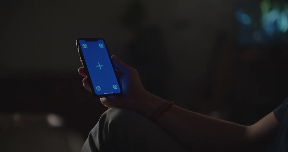 Man with black t shirt and pants sits on couch using smartphone in living room at home