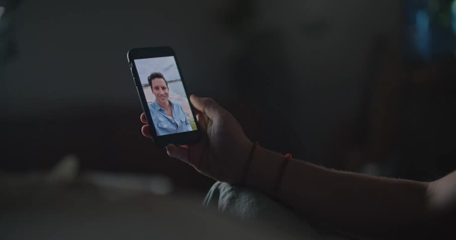 Man sitting on couch makes a video call on smartphone with man on the beach