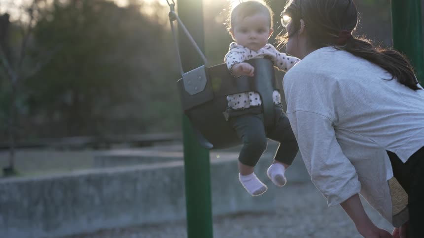 A woman kisses her daughter as she swings in a baby swing
