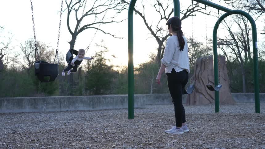 A woman pushes her baby in a swing at the park