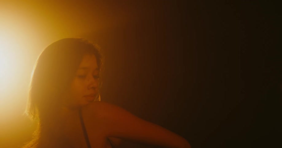Woman dancing alone at an empty dark room with an orange backlight