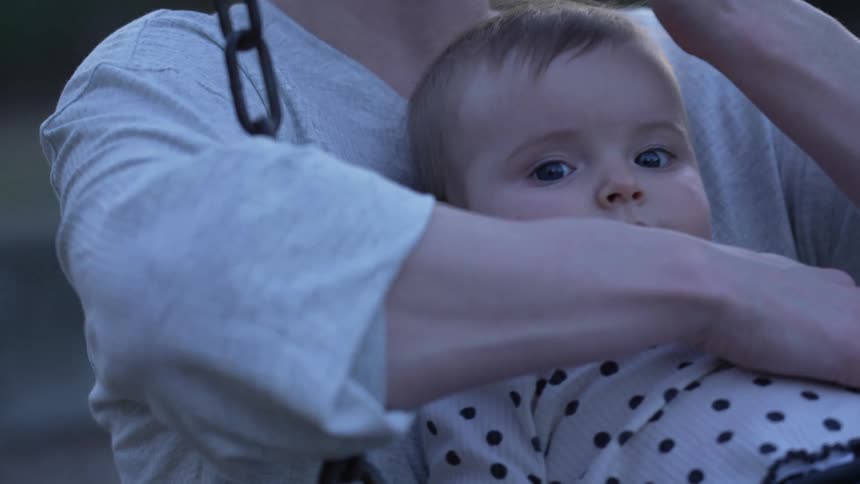 A woman holds her baby while swinging on a swing