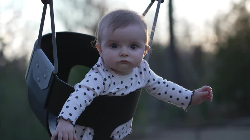 A woman pushes her daughter in a baby swing at the park