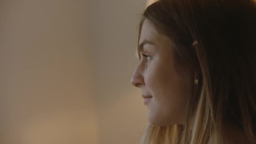 A woman smiles to herself while sitting in her bedroom thinking about the future