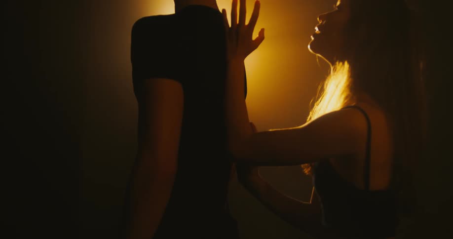 Woman stands behind a man and slides her hand and arm up the middle of his back