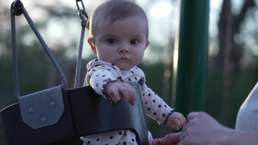 Serious baby looking at the camera swinging in a bucket swing