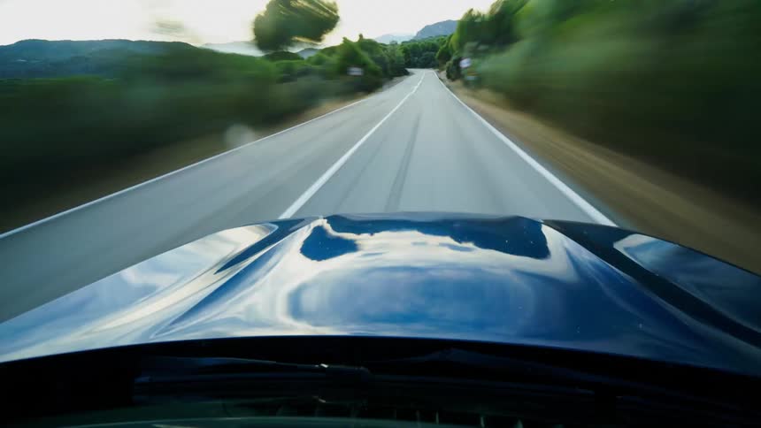 Blue car drives on country road at sunset