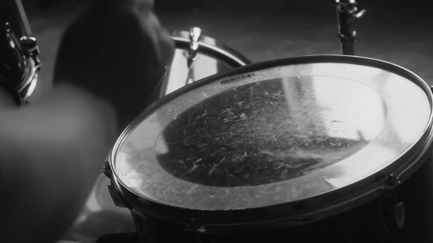 A man taps his knee and hits a drum with his drum stick