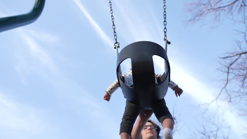 Mother with glasses swings baby in swim in playground