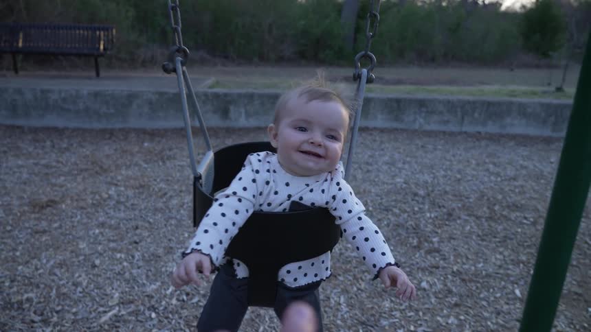 Mother swings baby in a swim in playground