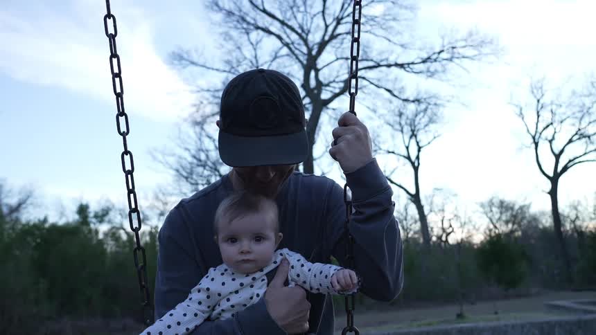 Smiling father holds child as they swing in park and car passes in background