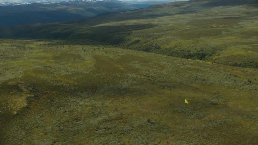 A helicopter flies over grassy hills