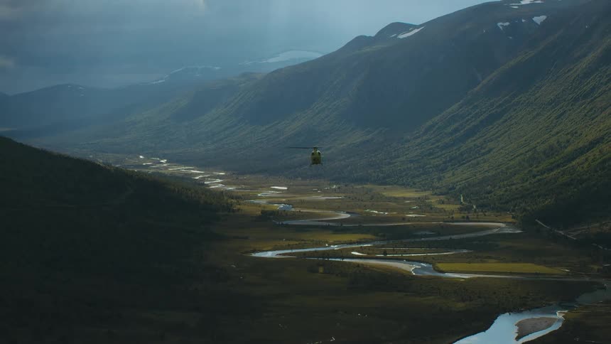 A helicopter flies above a creek in the valley of a canyon