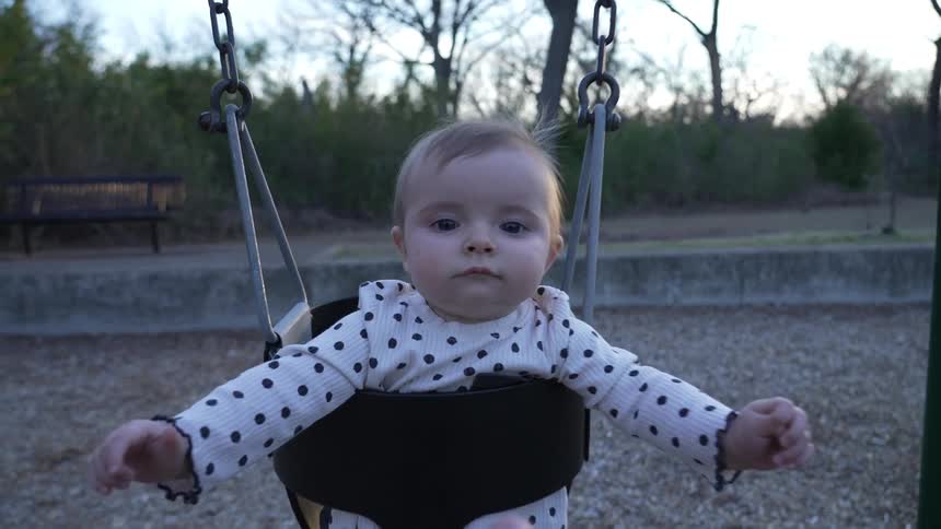 A baby swings in a swing and her mother gives her a push