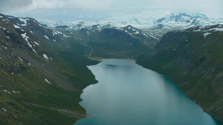 Snow dapples slopes near still water and covers mountains stretching toward the horizon in the background