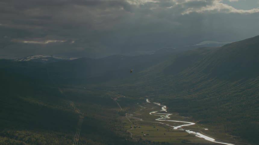 A helicopter flies over a verdant mountain valley on a cloudy day
