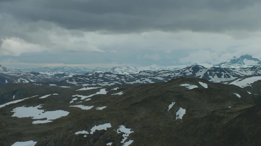 A mountainous countryside covered in patches of snow under a cloudy daytime sky