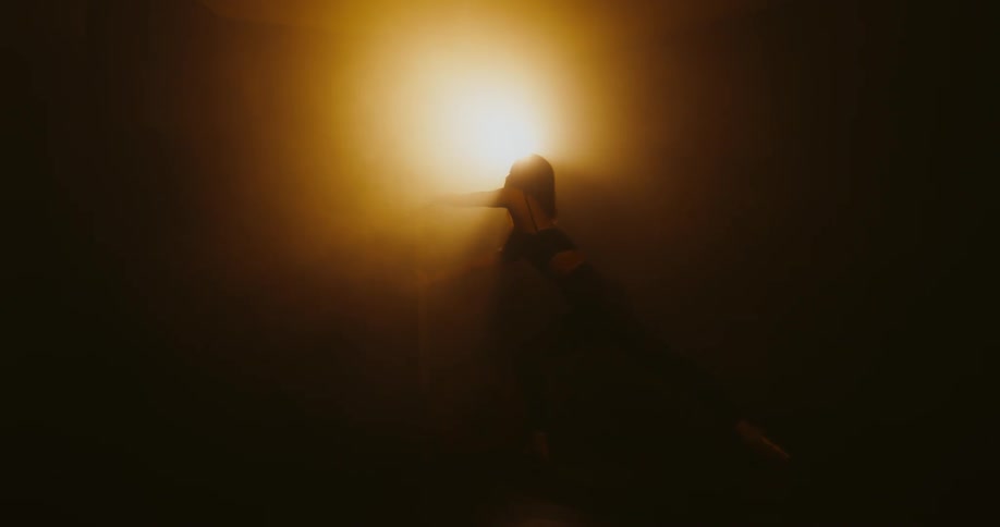 Ballerina moves through dance poses in darkness back lit by amber spotlight