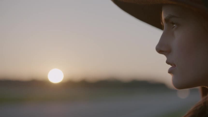 A woman is outside looking over a field at sunset