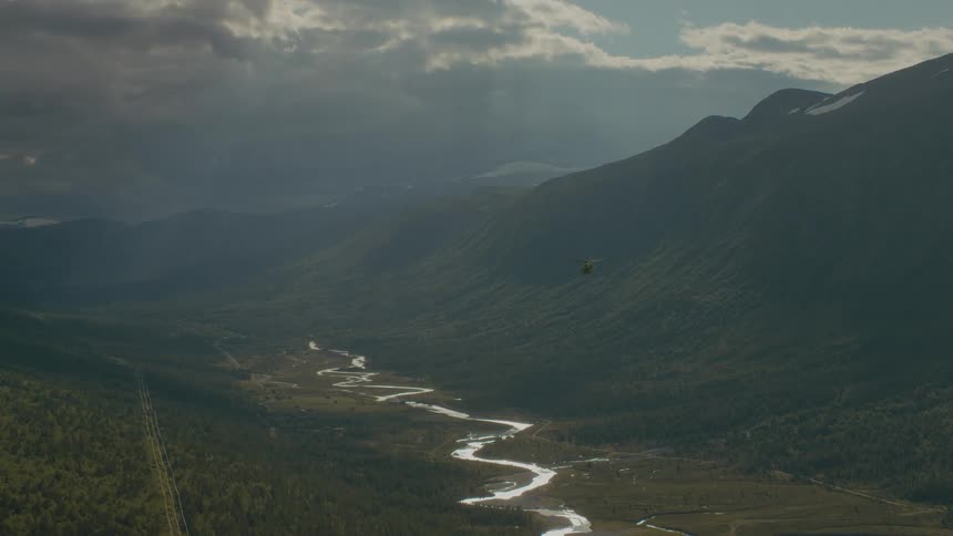 A helicopter flies over a river in a valley