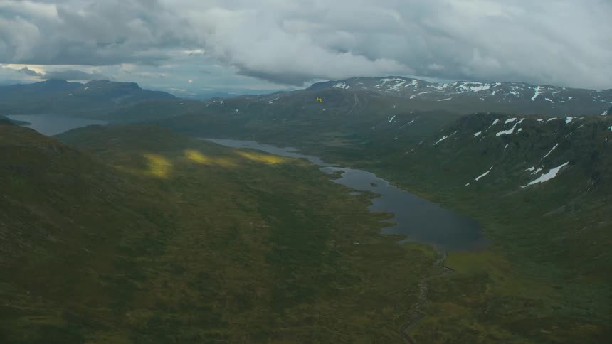 Person para sails over snow dappled mountains surrounding water under a very cloudy sky