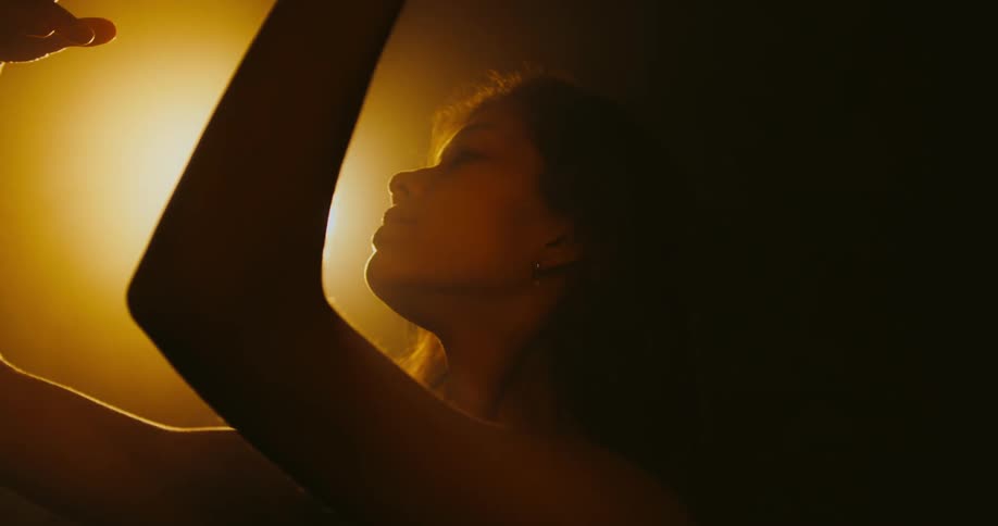 Woman moves her arms and hands while dancing under a bright light