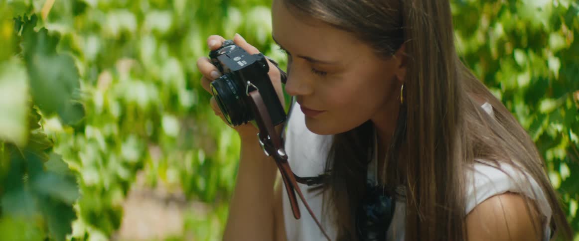 A woman wearing a camera around her neck shoots photos in a garden