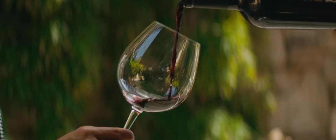 Person holds wine glass as red wine is poured into it