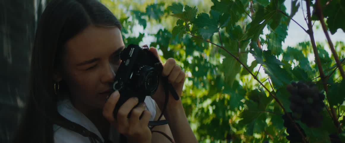 A woman takes a photo of grapes on the vine with her camera