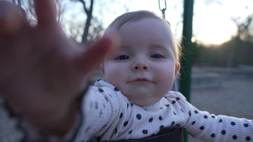Mother swings baby in swing in playground at sunset