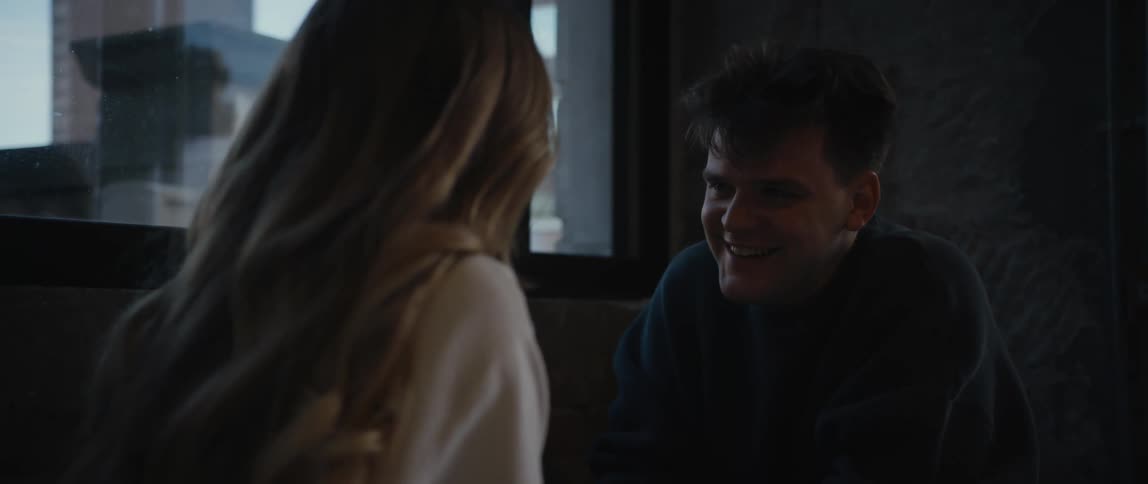 A man is sitting down in a booth talking to a woman and he has a big smile on his face