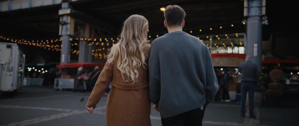A man and woman walk outdoors while holding hands during the day