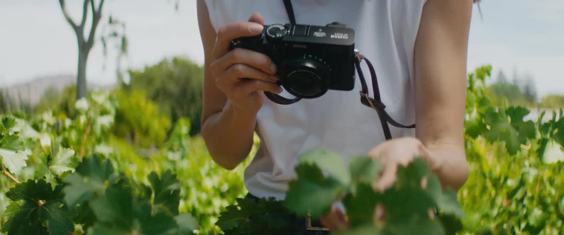 Photographer stands outdoors in garden before taking pictures with her camera