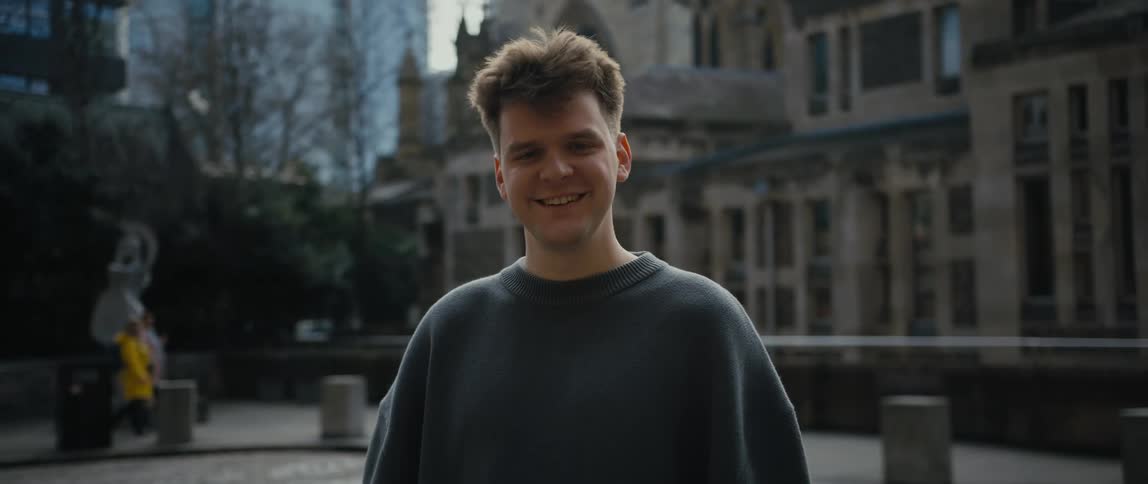 Man wearing a sweatshirt smiling while standing in front of a historical building