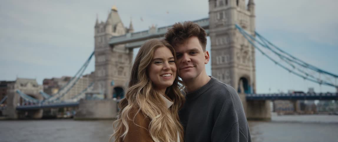 Man and woman touching their heads and posing for a picture in front of a bridge