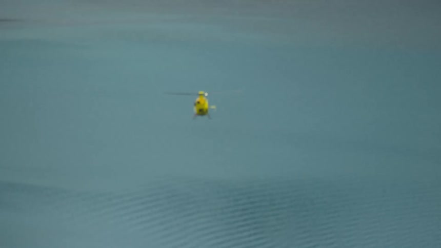 Yellow helicopter flying across the ocean